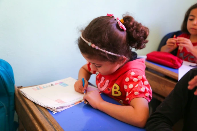 A little girl sitting at a desk writing on a piece of paper